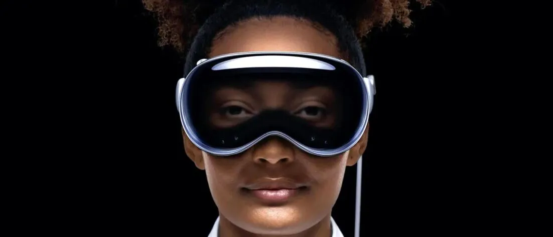 Marketing photo of a black woman wearing Apple Vision Pro spatial computing device where you can see her occluded eyes via the curved OLED panel in the front making it look like she's looking through a clear pair of goggles
